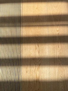 Wooden flooring with alternating vertical slats on the left side. Shadows cast across the surface, creating a pattern of light and dark bands.