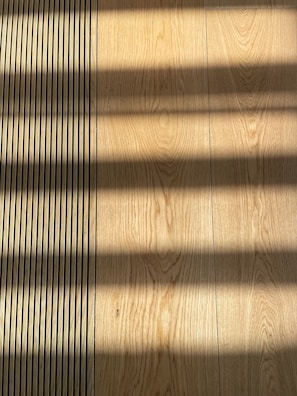 Wooden flooring with alternating vertical slats on the left side. Shadows cast across the surface, creating a pattern of light and dark bands.