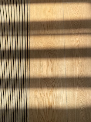 Wooden flooring with alternating vertical slats on the left side. Shadows cast across the surface, creating a pattern of light and dark bands.