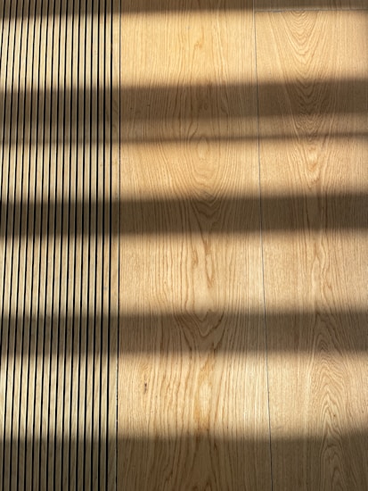 Wooden flooring with alternating vertical slats on the left side. Shadows cast across the surface, creating a pattern of light and dark bands.