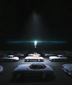 A group of retro cars lined up against a backdrop of a starry night sky and a giant rocket sculpture.