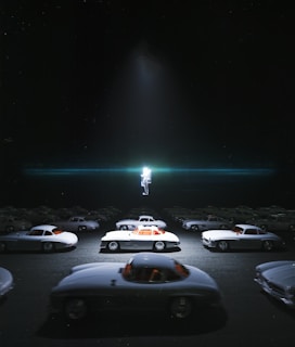 A surreal scene depicting a large collection of vintage sports cars arranged on a flat surface under dim lighting, with a glowing astronaut figure hovering above them in the center. The cars are primarily white with contrasting red interiors, and the entire setting is enveloped in darkness except for a focused beam of light on the astronaut, adding to the mysterious ambiance.