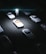 A dark parking lot with multiple vintage white cars evenly spaced, illuminated by a strong central light. In the spotlight stands a figure in a reflective astronaut suit, casting a glowing presence amidst the surrounding darkness.