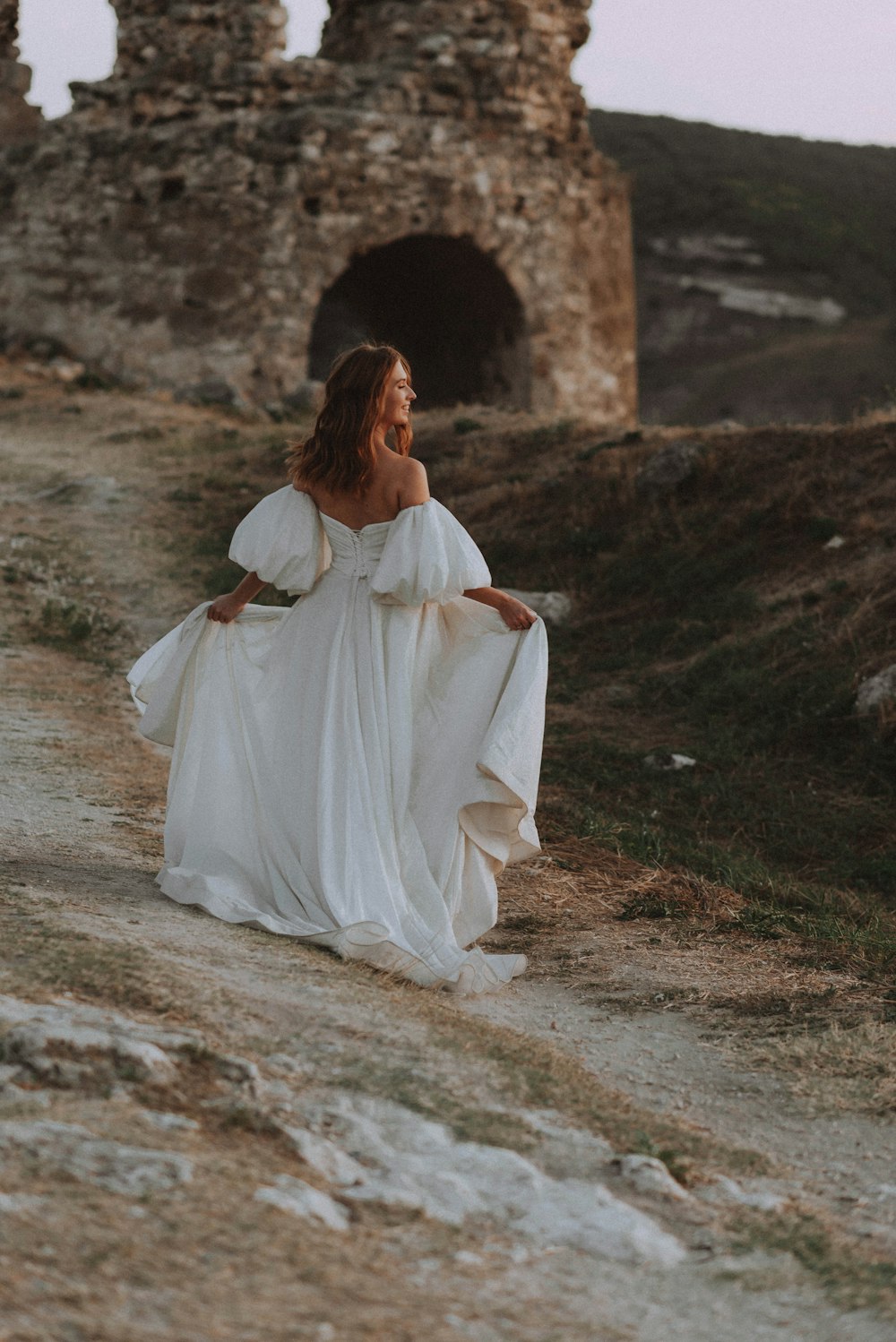 a woman in a white dress walking down a dirt road