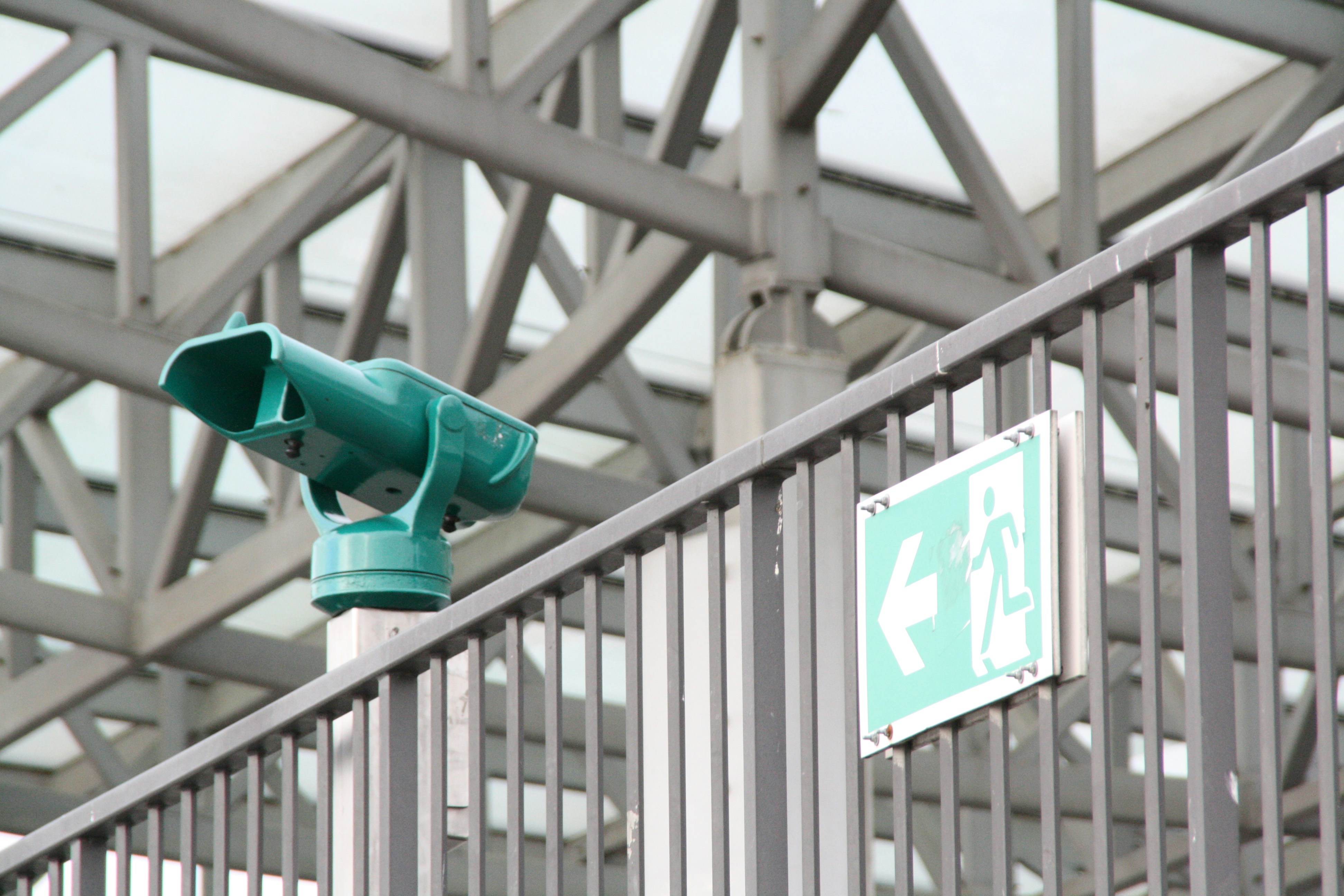 a green traffic light mounted to the side of a metal fence