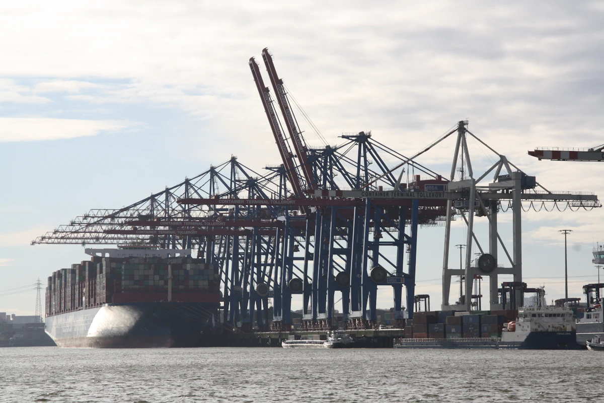Container ship docked at a quay with gantry cranes — the berth-toe environment where Texas Tuff Rock Bags interrupt the scour mechanism that undermines the wall