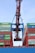 A large industrial crane is positioned over a stack of colorful shipping containers, lifting one container. The containers are branded with various shipping company names and appear to be part of a busy port operation.