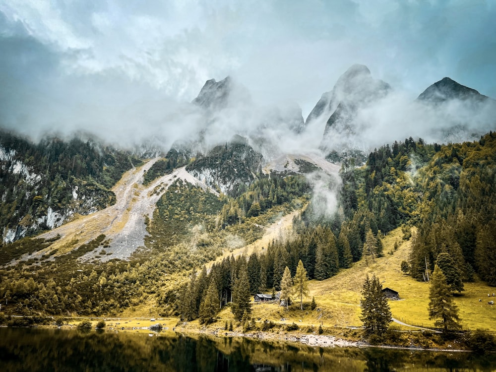 a mountain covered in fog and clouds next to a body of water