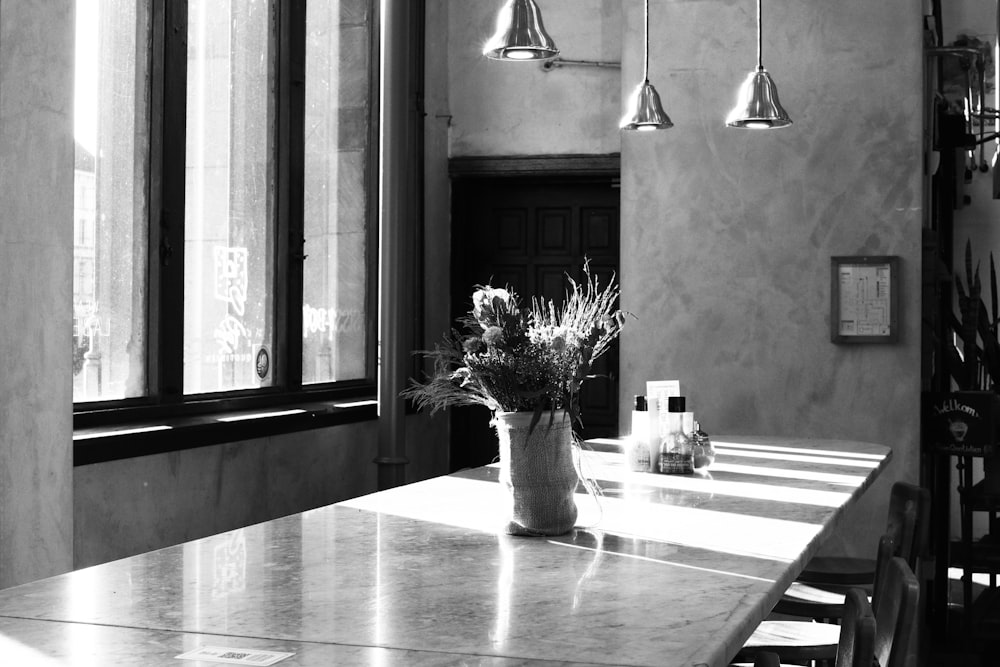 Une photo en noir et blanc d’une table avec un vase de fleurs