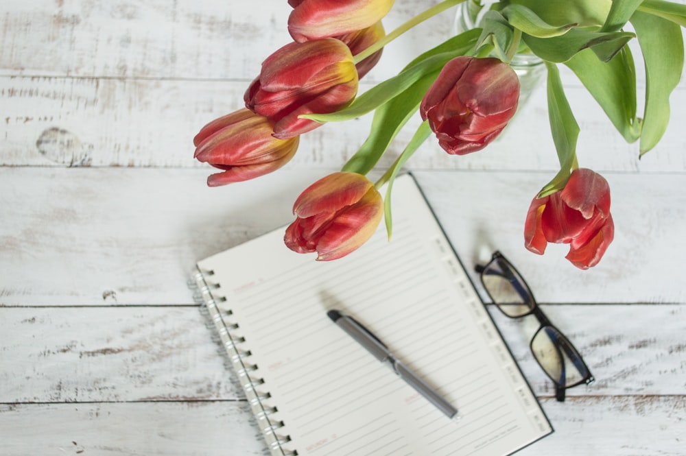 a notepad, pen, glasses and tulips on a white wooden table