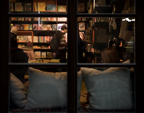Warm-lit bookstore interior with customers browsing and chatting among shelves.