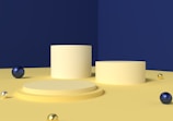 Several cylindrical platforms arranged on a flat surface with a deep blue wall in the background. There are multiple metallic spheres of varying sizes scattered on the surface, with colors including gold, blue, and silvery white.