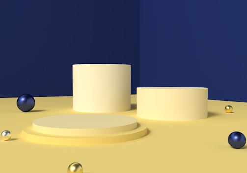 Several cylindrical platforms arranged on a flat surface with a deep blue wall in the background. There are multiple metallic spheres of varying sizes scattered on the surface, with colors including gold, blue, and silvery white.