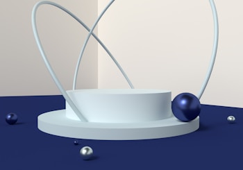 A minimalist geometric design featuring a round platform with multiple blue and silver spheres of varying sizes. Quietly intersecting the platform are thin, curved rods that form abstract loops. The setting uses muted tones with a soft gradient wall, combining cream and navy colors, creating a modern and sophisticated atmosphere.