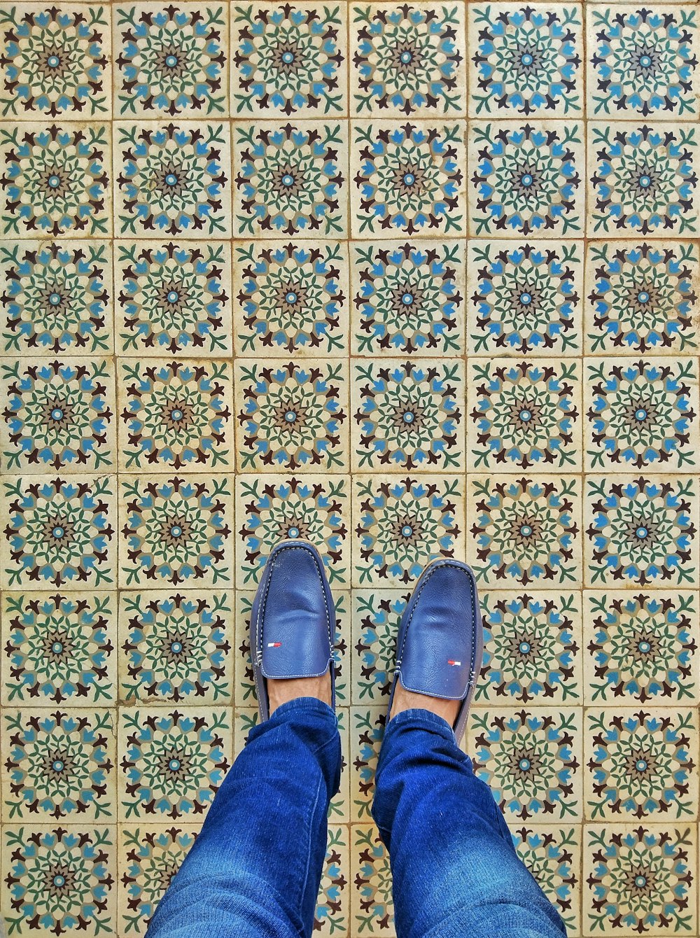 a person standing on a tiled floor with blue shoes
