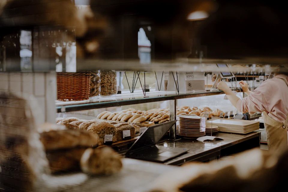 Mostrador de una panadería con hogazas recién horneadas y una persona atendiendo al fondo.