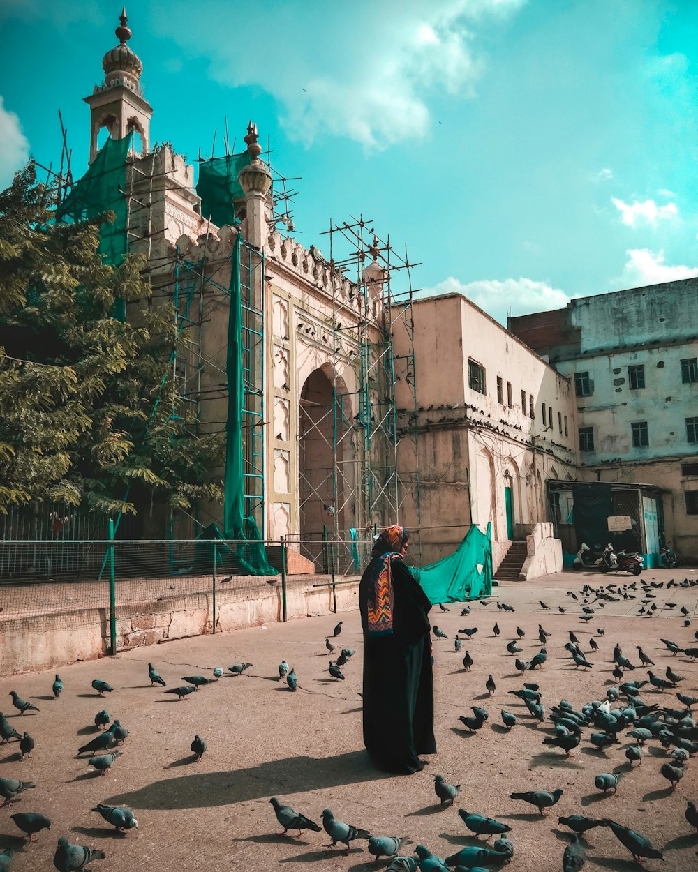 a woman standing in front of a building surrounded by pigeons