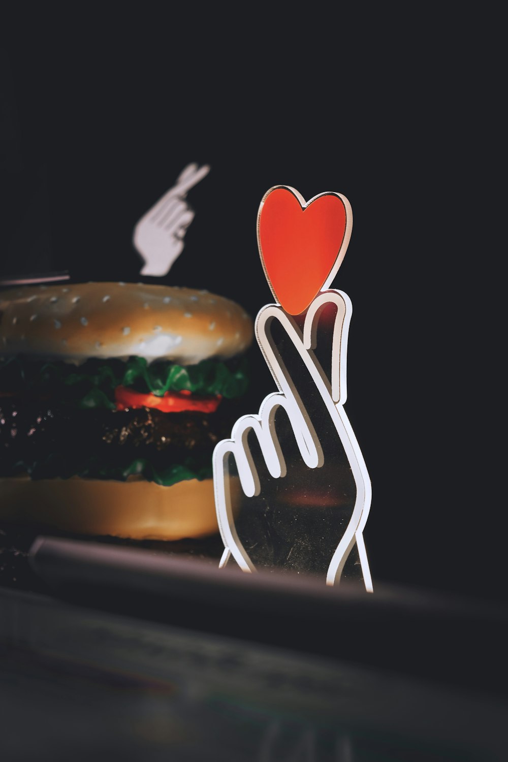 une main tenant un papier en forme de cœur découpé dans un hamburger