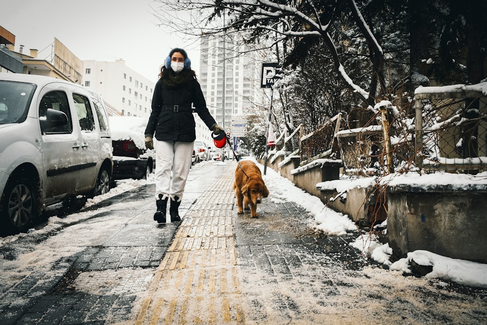 a woman walking a dog on a snowy sidewalk