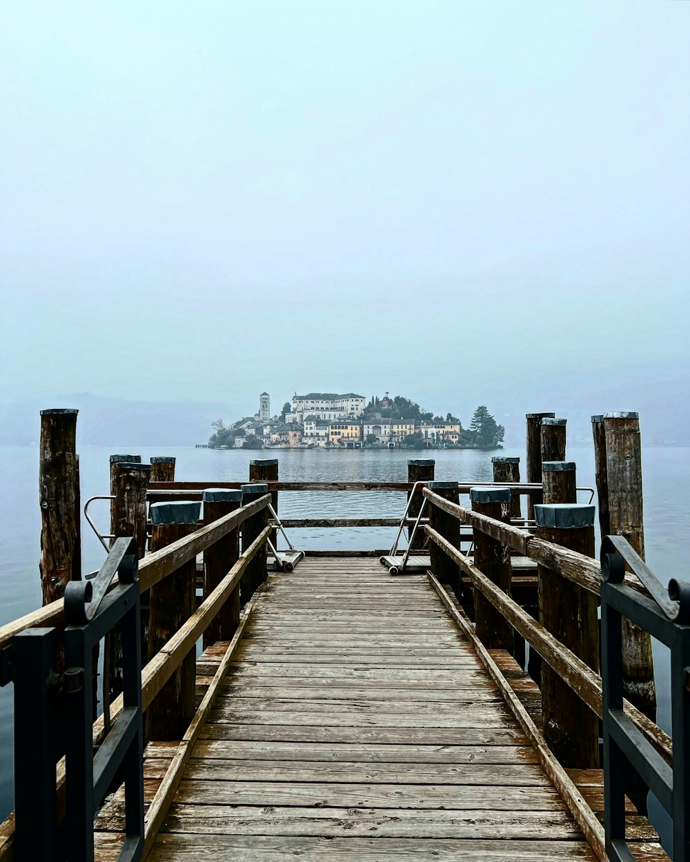 a wooden pier with a view of a large island in the distance