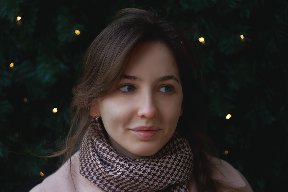 a woman wearing a scarf in front of a christmas tree