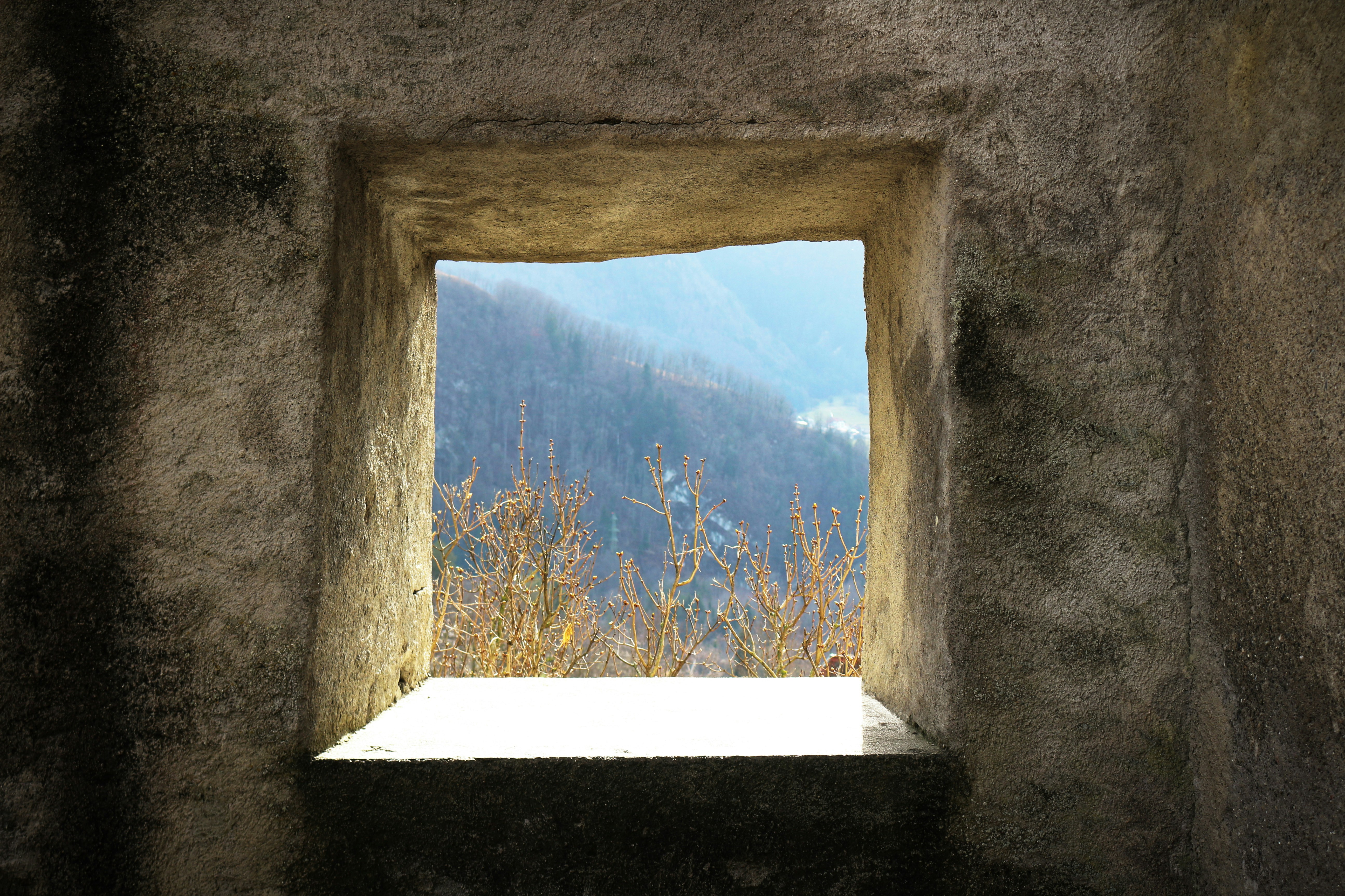 a window in a stone wall with a view of a mountain