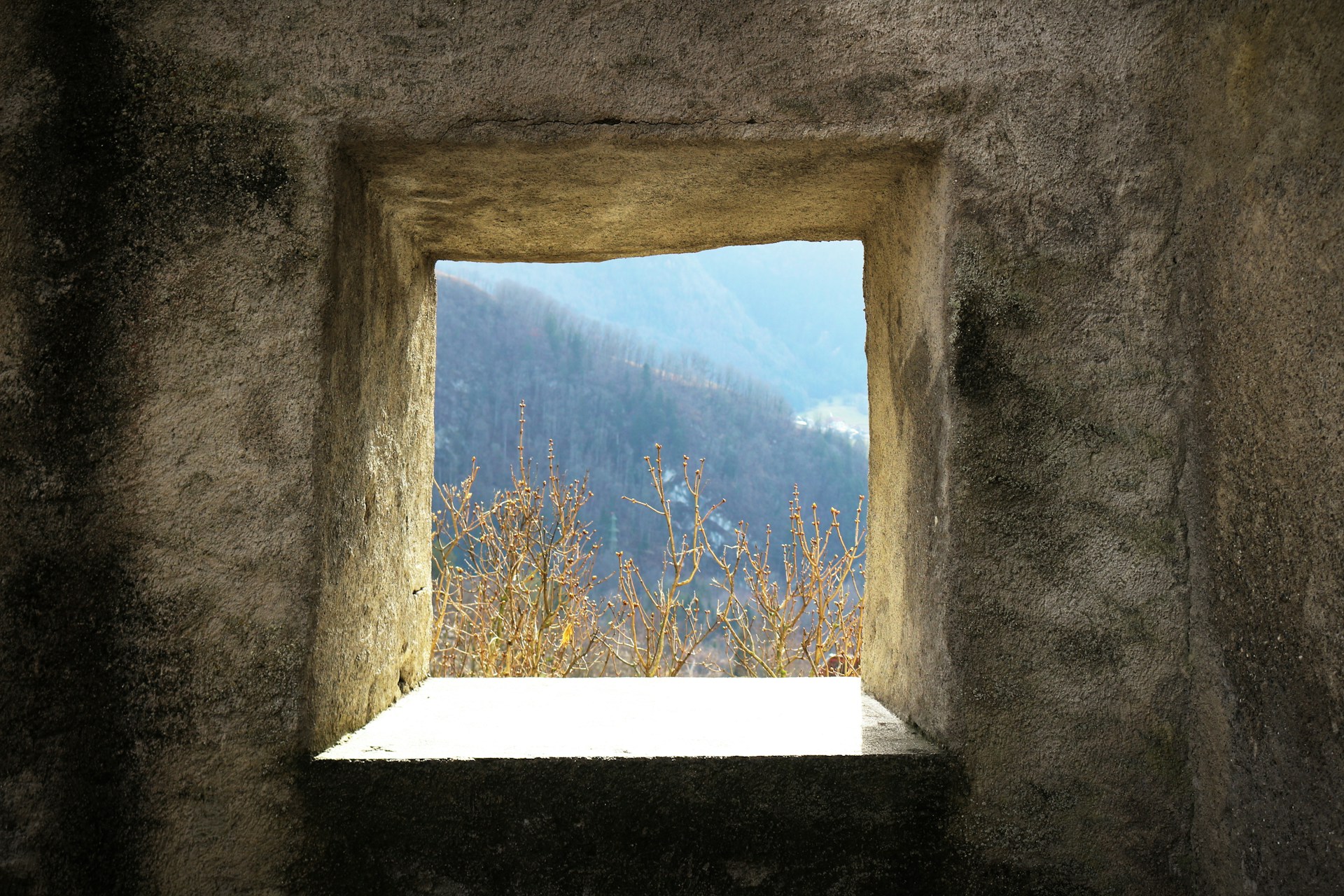 a window in a stone wall with a view of a mountain
