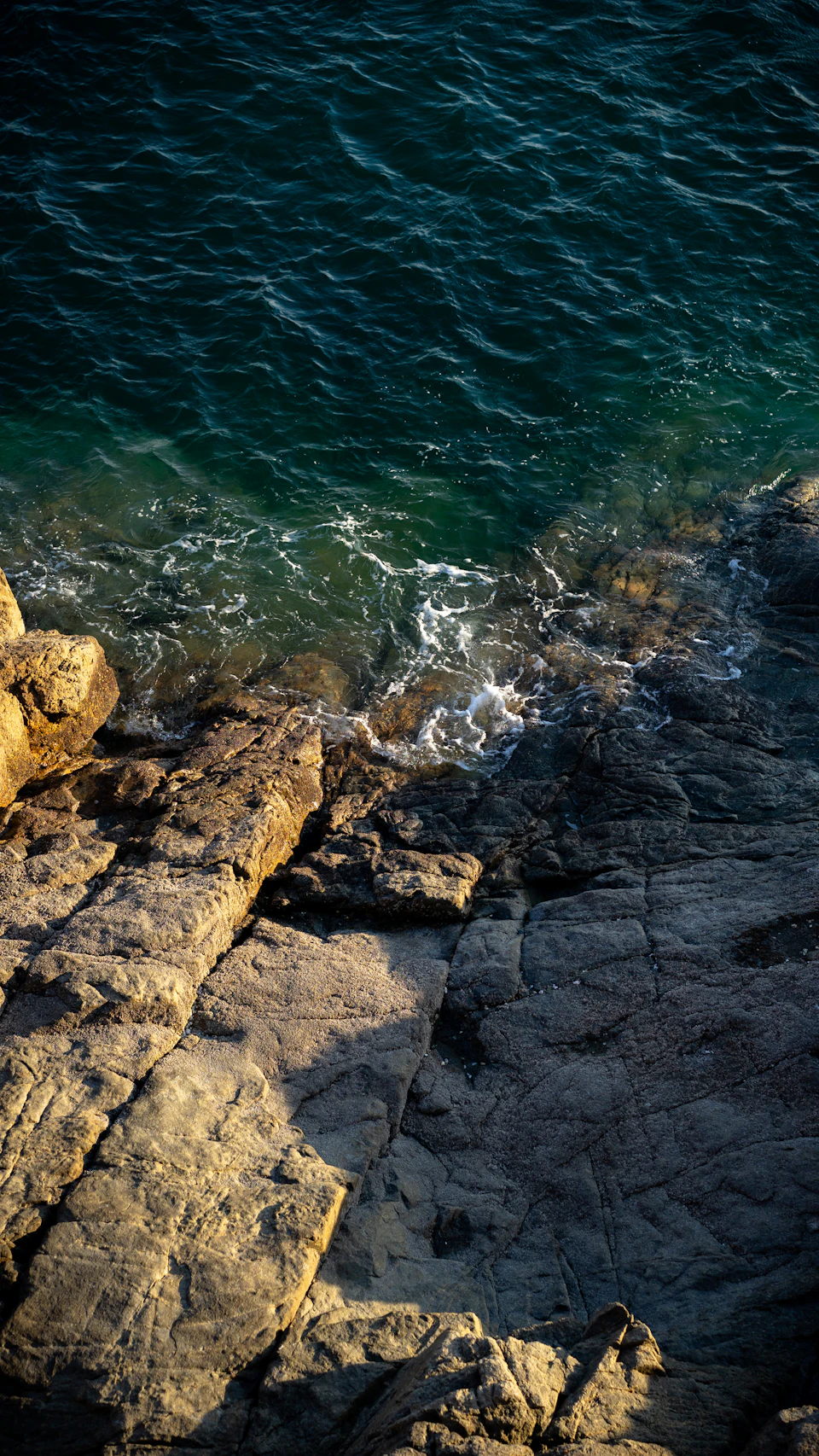 Rocky cliff overlooking a body of water with ocean's surface reflecting the sky above