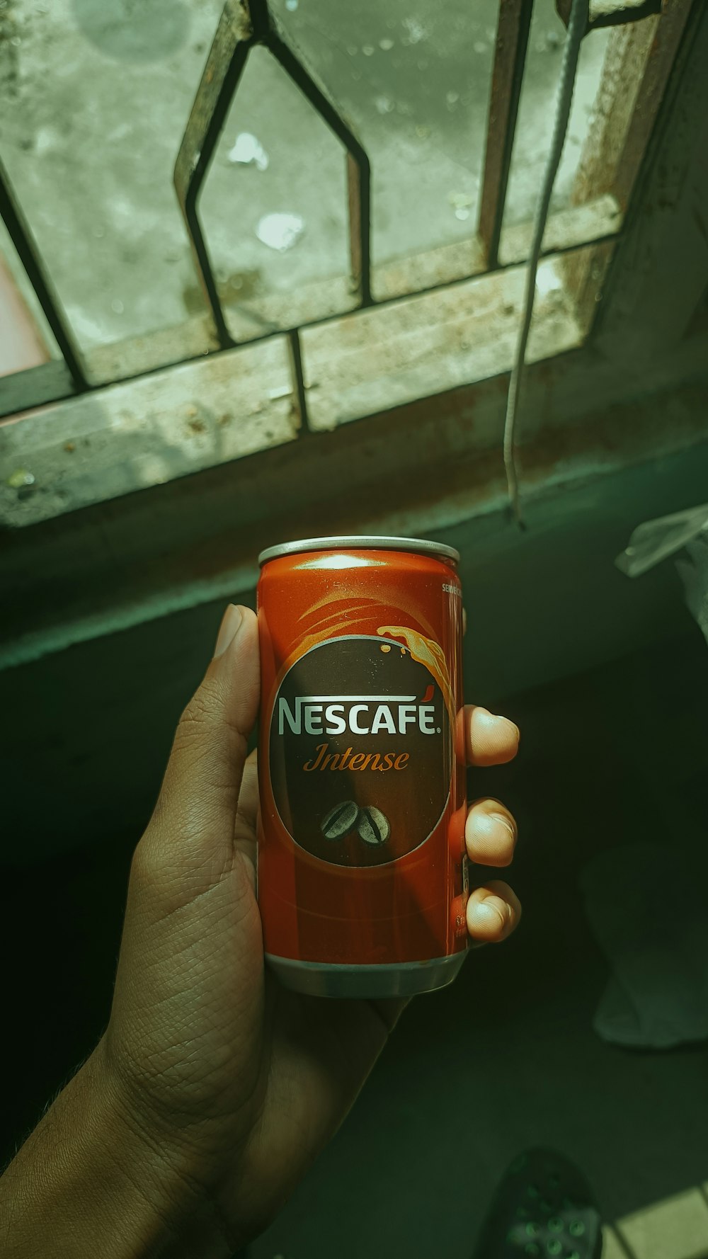 a hand holding a can of coffee in front of a stained glass window
