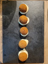 A rustic wooden board with crispy patatas bravas topped with spicy red sauce and a side of golden croquetas