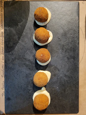 A rustic wooden board with crispy patatas bravas topped with spicy red sauce and a side of golden croquetas