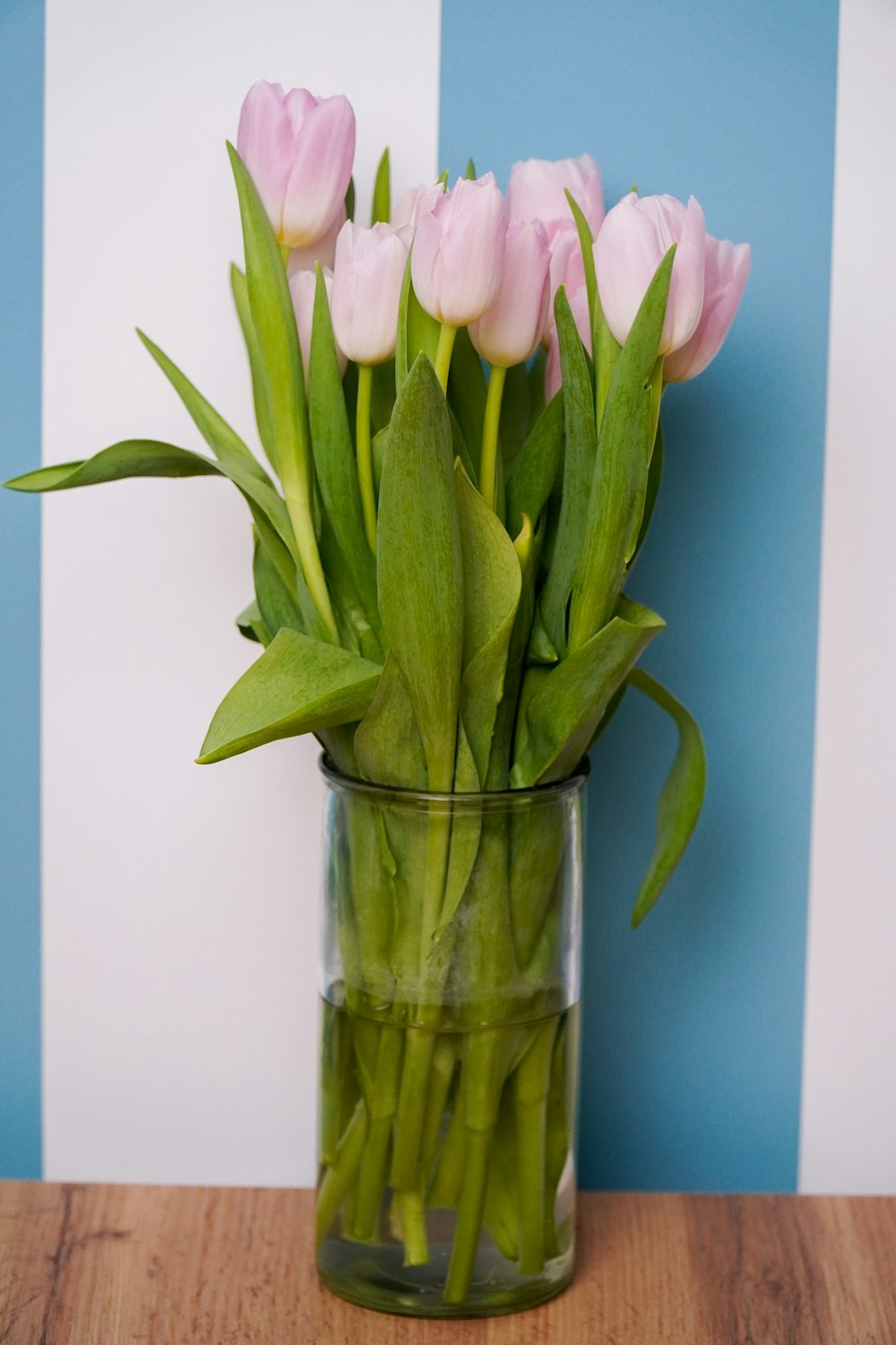 Un jarrón de vidrio lleno de tulipanes rosados sobre una mesa