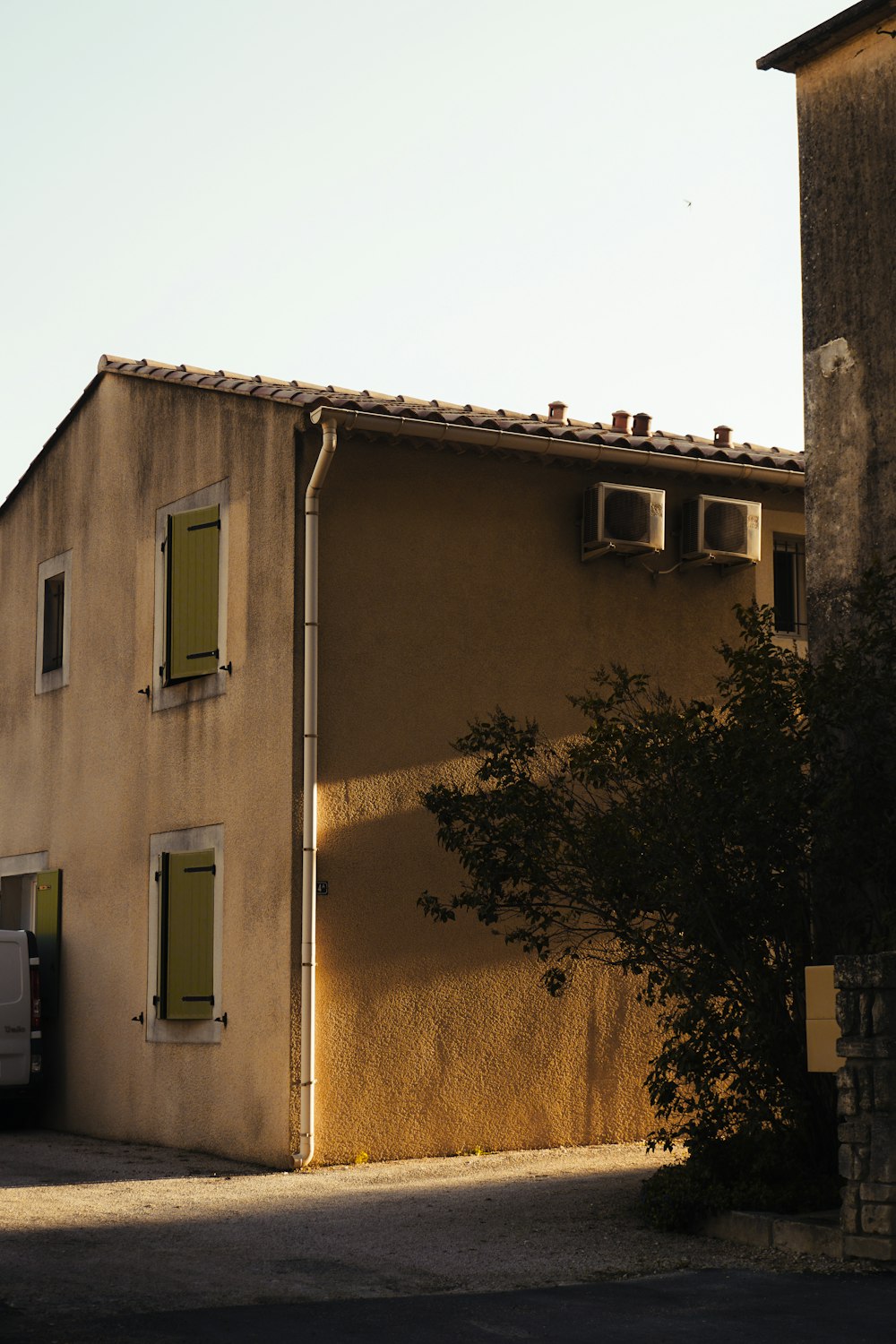 a tan building with two windows and a tree in front of it