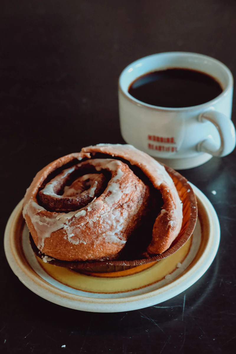A cinnamon roll on a plate next to a cup of coffee
