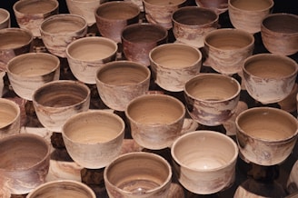 Numerous ceramic bowls with a marbled pattern in shades of brown and beige are arranged closely together. The bowls have a rustic appearance and vary slightly in color and texture, suggesting handmade craftsmanship.