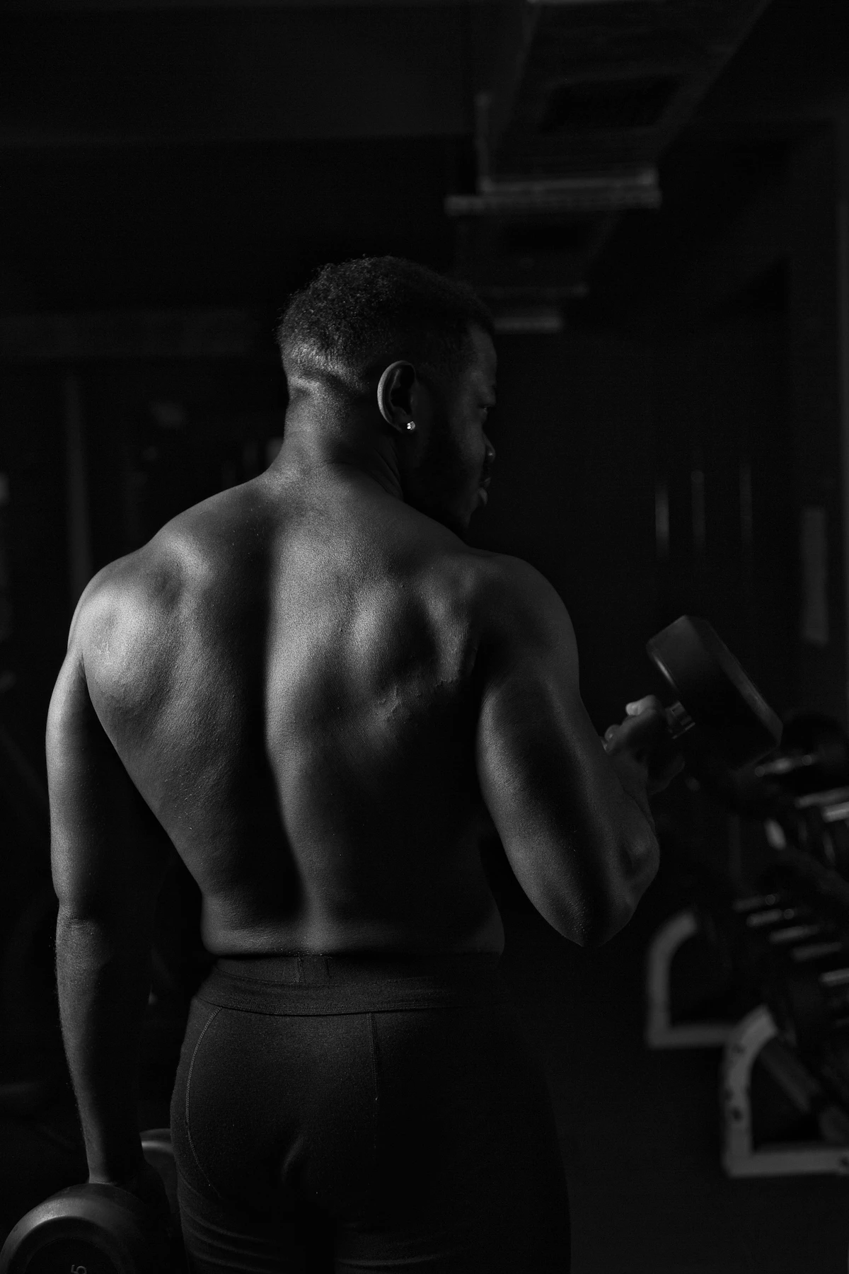 Man training with a barbell in low light, illustrating a strength athlete weighing peptides versus anabolic steroids.