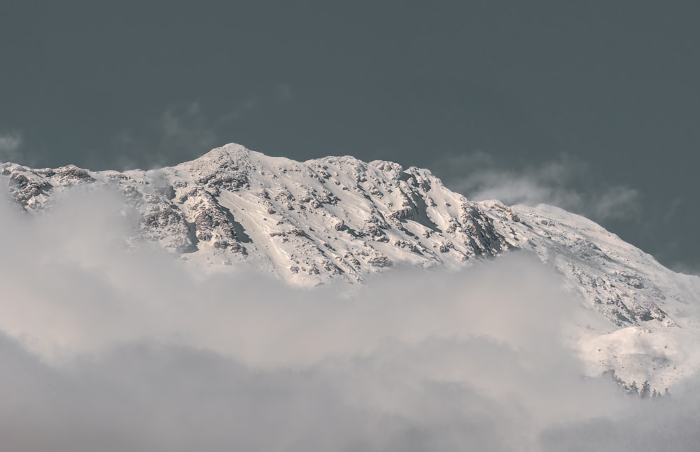 a mountain covered in snow and clouds under a gray sky