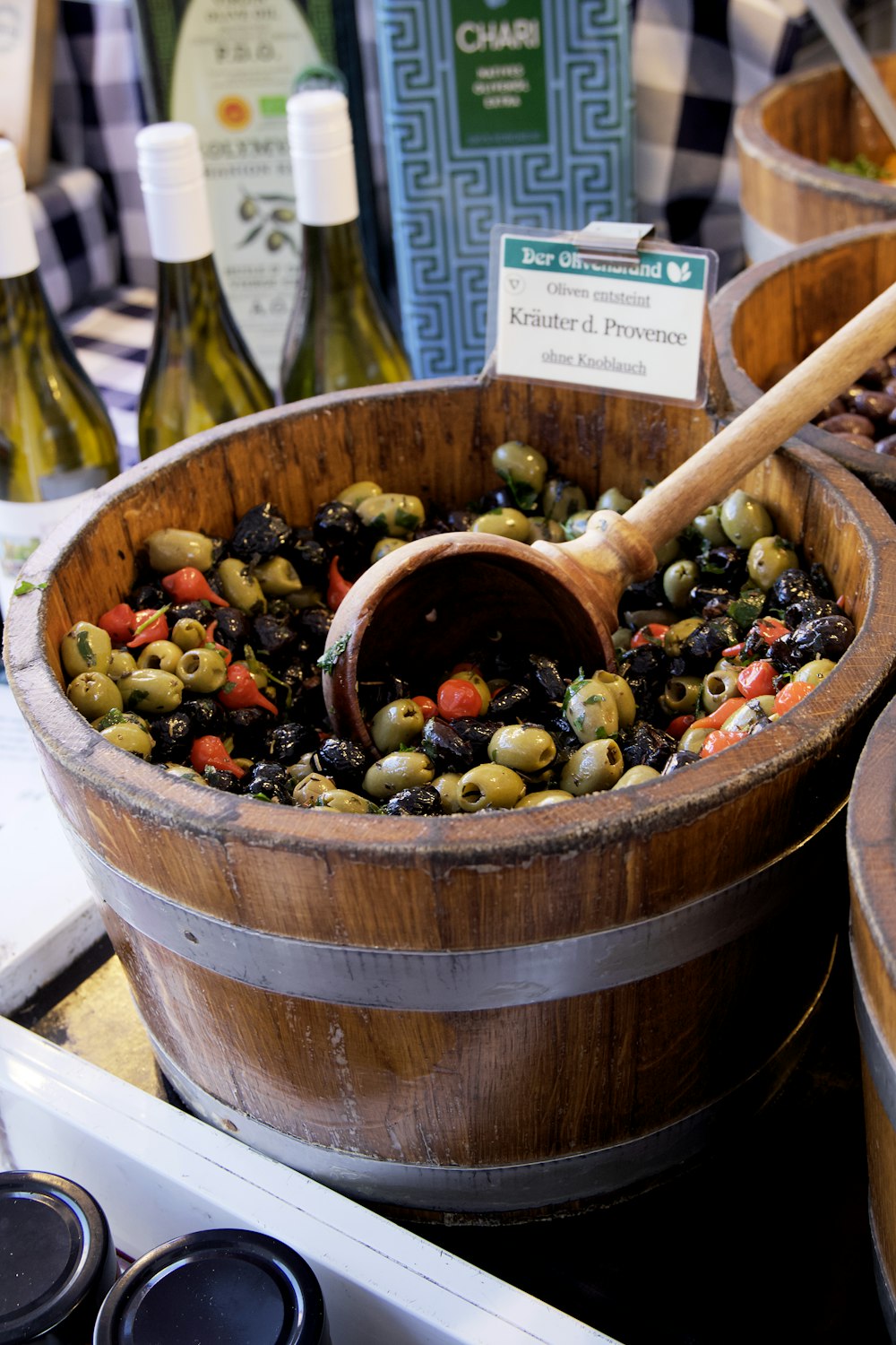 a wooden bucket filled with olives next to bottles of wine