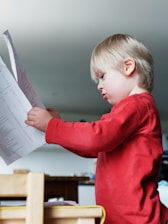 a young boy reading a paper while sitting at a table