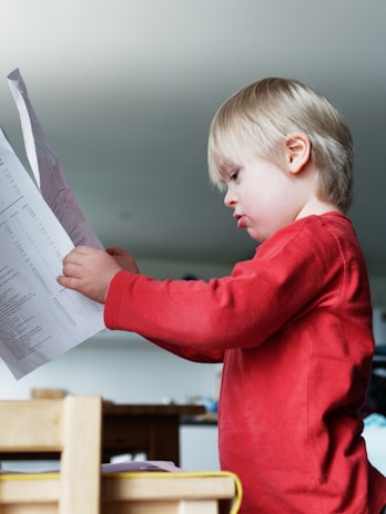a young boy reading a paper while sitting at a table
