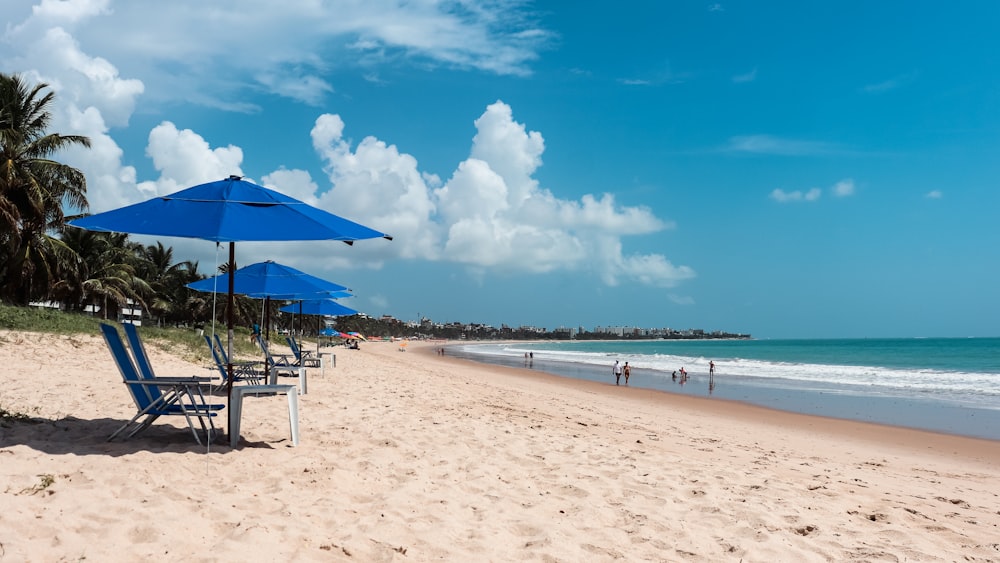 a beach with blue umbrellas and people in the water