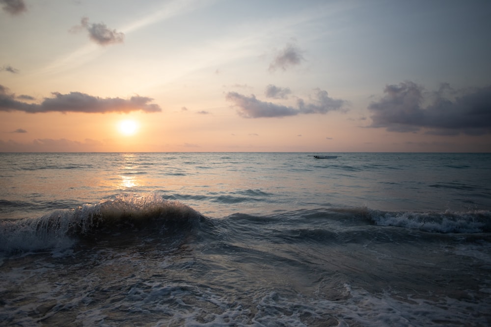 the sun is setting over the ocean with a boat in the distance