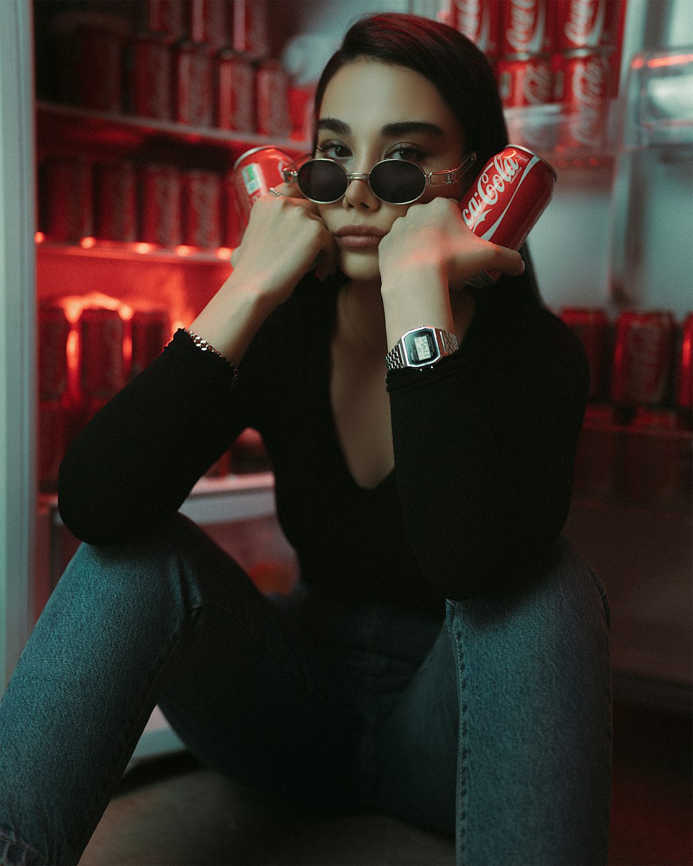 a woman sitting in front of a refrigerator holding a can of soda