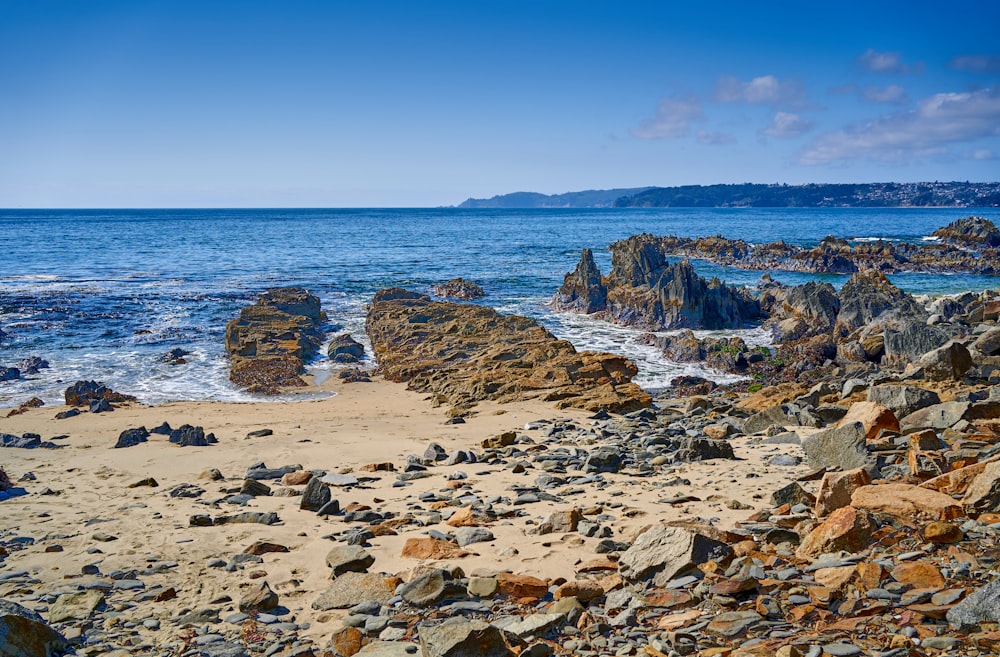 a sandy beach with rocks and water in the background