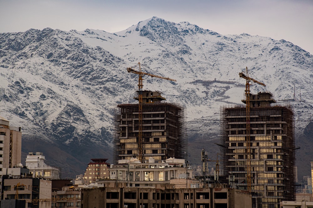 a group of tall buildings in front of a snow covered mountain