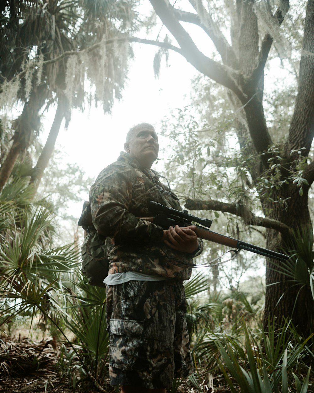 a man holding a rifle in a forest