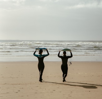 two people walking on a beach carrying surfboards