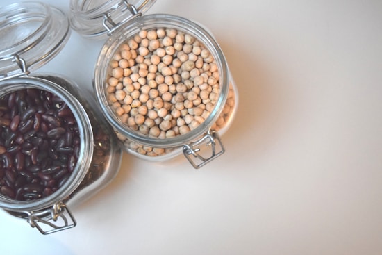 Two glass jars with hinged lids are filled with chickpeas and dark red kidney beans. The jars are placed on a smooth, off-white surface, with both lids partially open.
