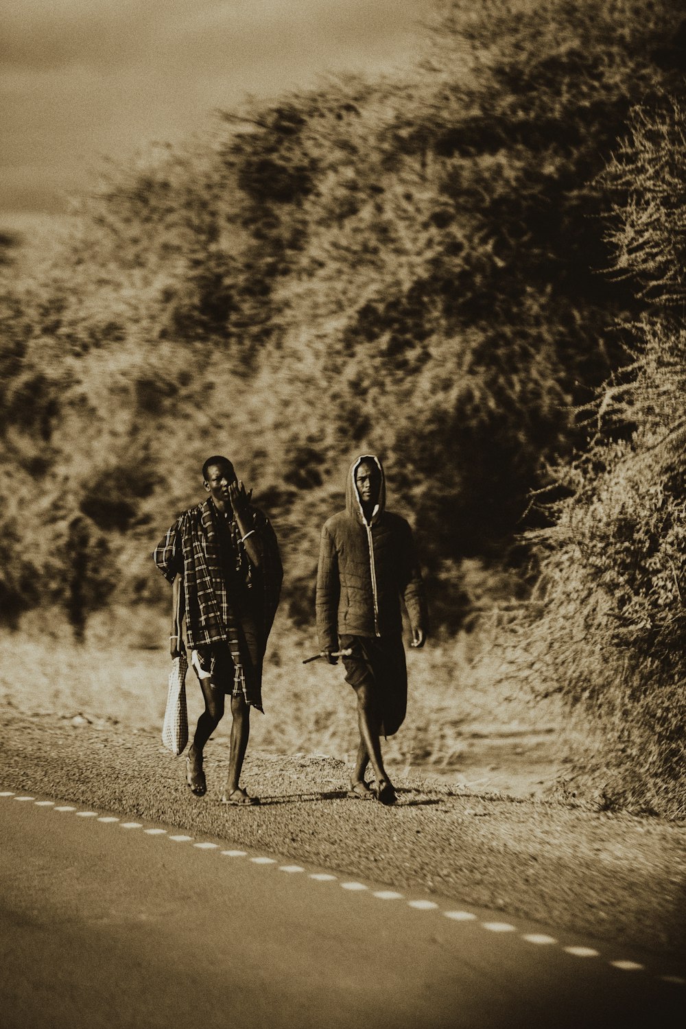 two people walking down a road with a hill in the background