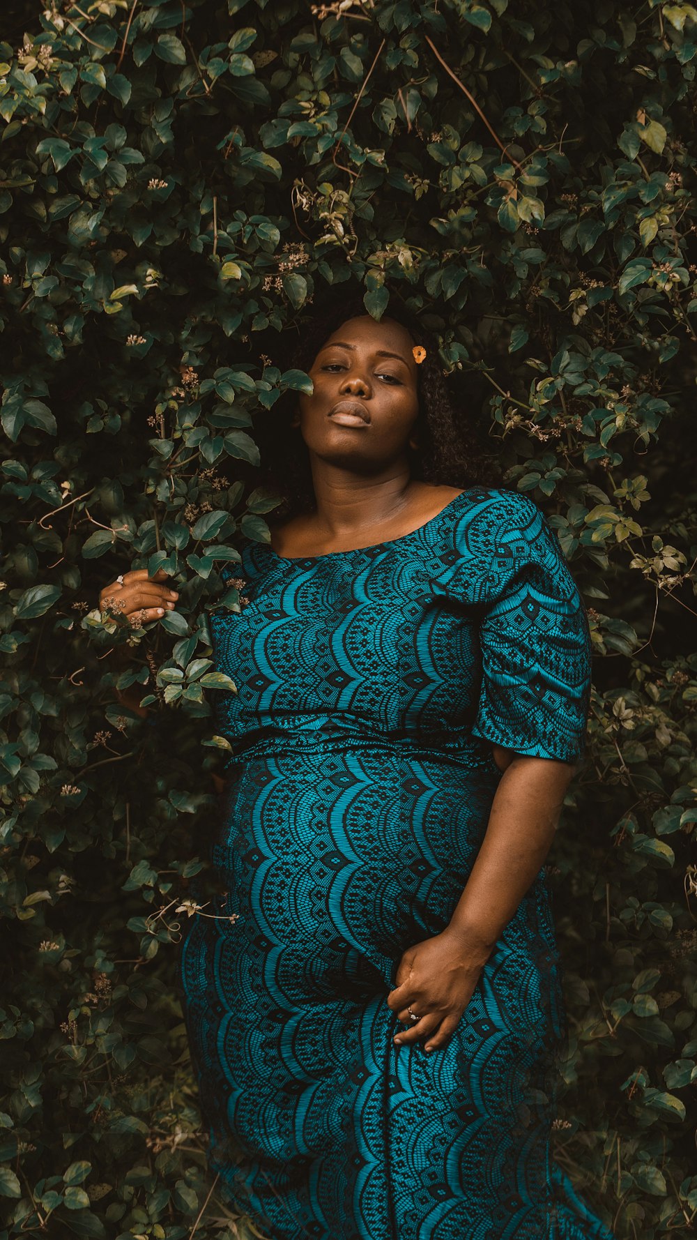 a pregnant woman standing in front of a bush